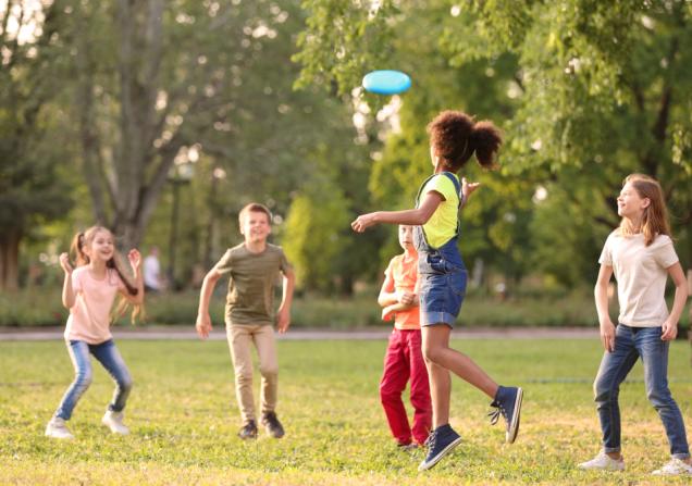 A group of 5 children playing frisbee in a park on a sunny day. Image by New Africa via Shutterstock.