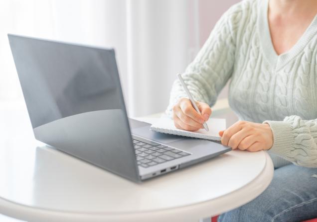 Woman behind her laptop with a pen and note paper. Image by CeltStudio via Shutterstock