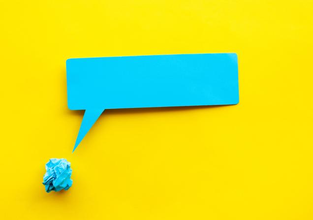 An empty bright blue speech bubble emerges from a ball of screwed up paper in the same colour. The background of the image is bright yellow. Image by HAKINMHAN via Shutterstock.