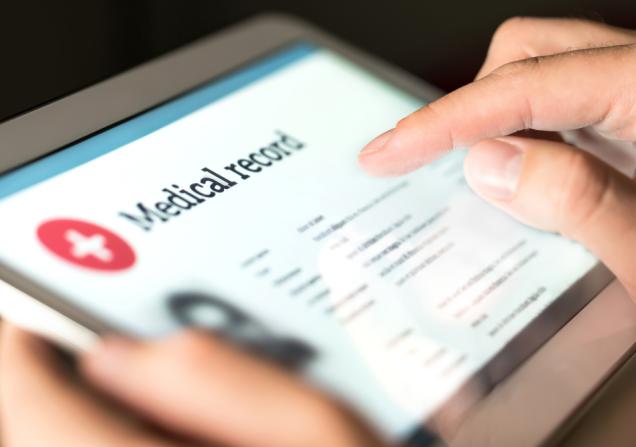 A close-up of a person holding a tablet. They are looking at their medical records. Image by Tero Vesalainen via Shutterstock.