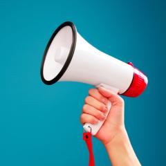 A picture of a hand holding up a megaphone against a turquoise background. Image by Sergey Mironov via Shutterstock