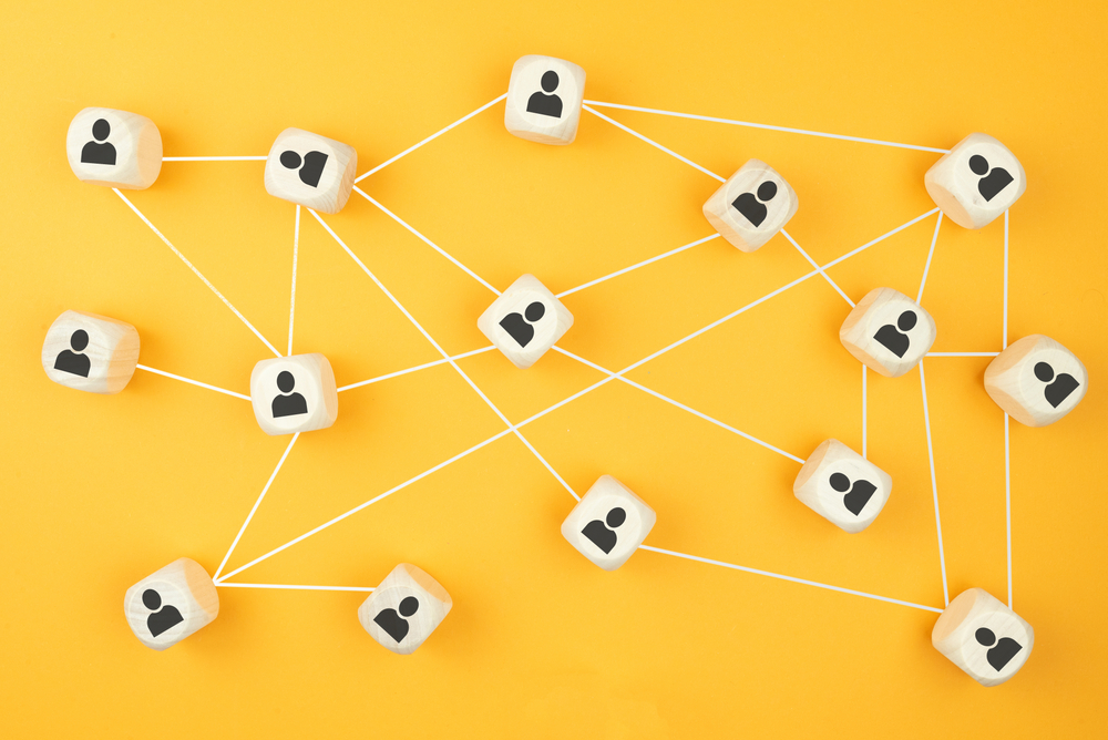 Wooden blocks with icons of people connecting by white lines, set against a bright yellow background. Image by Christian Horz via Shutterstock.