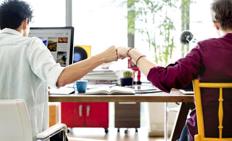 Two people fistbumping at a desk. Image courtesy of Rawpixel.com via Shutterstock