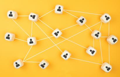 Image by Christian Horz via Shutterstock. Wooden blocks with icons of people connecting by white lines, set against a bright yellow background. Image by Christian Horz via Shutterstock.