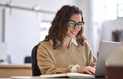 Smiling female student using computer technology learning online, doing web research.
