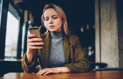 IMI projects are using smartphone apps to gather real time, reliable information on patients' health. Image by GaudiLab via Shutterstock. A young woman with a serious expression on her face is sitting at a table, using a smartphone. Image by GaudiLab via Shutterstock.