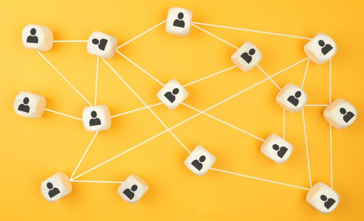 Wooden blocks with icons of people connecting by white lines, set against a bright yellow background. Image by Christian Horz via Shutterstock.