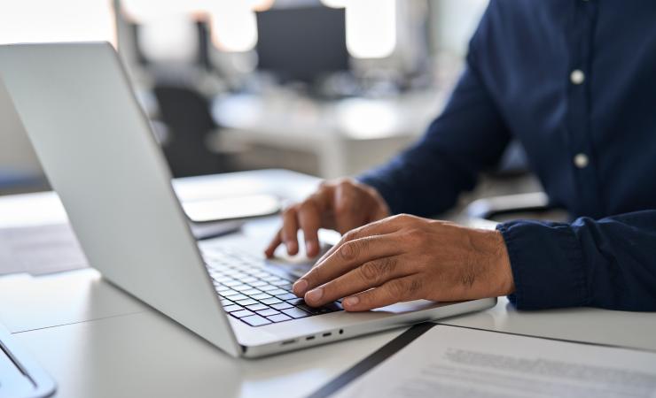 Bearded man hands typing on laptop keyboard.