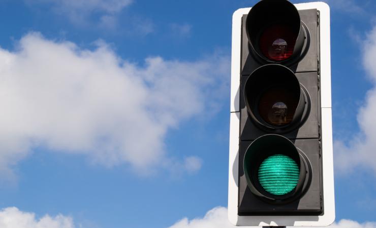 A green traffic light against a blue sky with a few fluffy white clouds. Image by Eddie J. Rodriquez via Shutterstock.