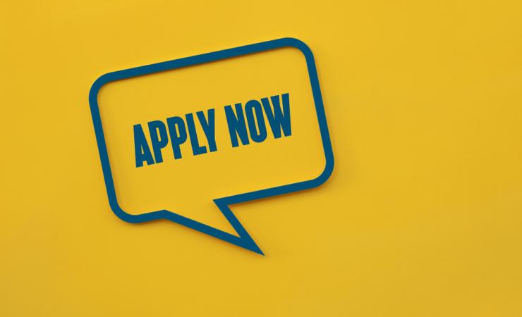 The words 'apply now' written in a speech bubble on a yellow background. Image by Marta Design via Shutterstock.