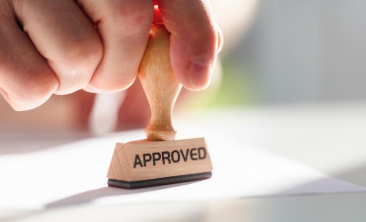 A hand stamping something with an 'APPROVED' stamp. Image by Brian A Jackson via Shutterstock.