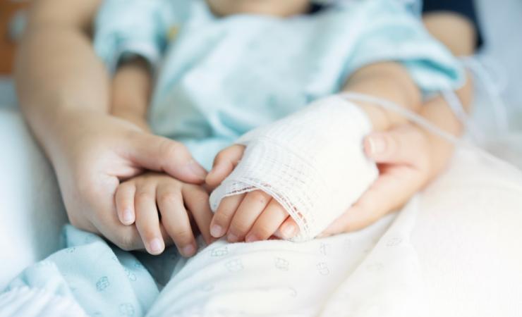 Close-up of a parent holding the hands of a child in a hospital - the child's hand is bandaged and has a drip. Image by Kunlathida6242 via Shutterstock.