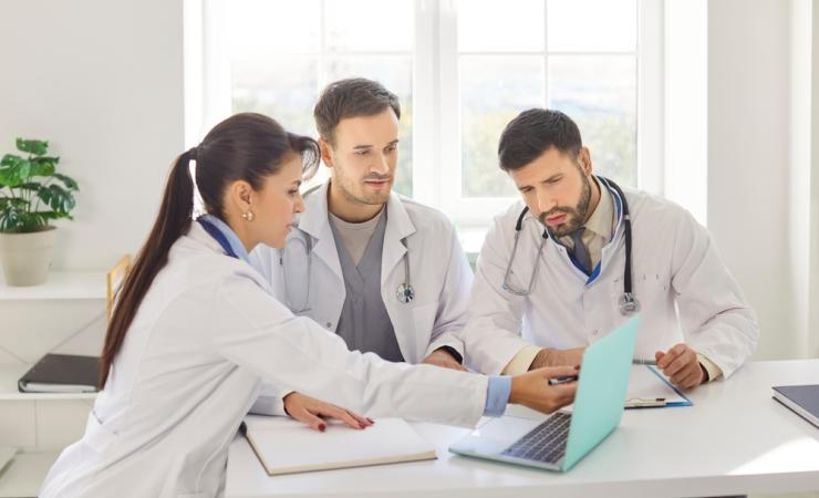 Three doctors discussing around a laptop. COMPASS aims to boost cardiology-oncology collaboration.