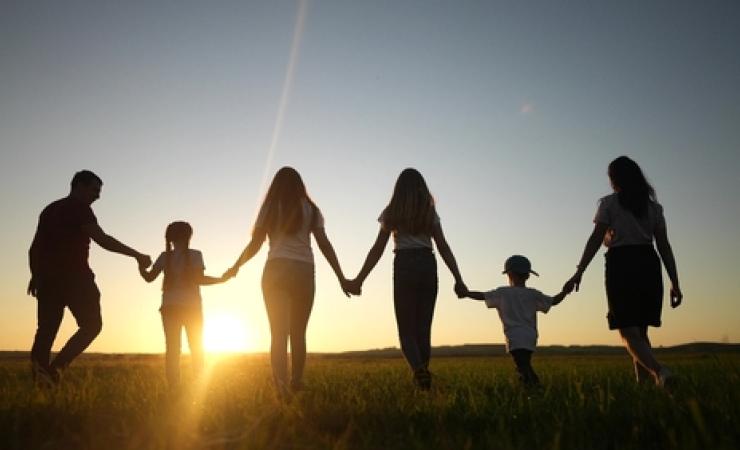 A group of people of all ages standing before a sunset. 