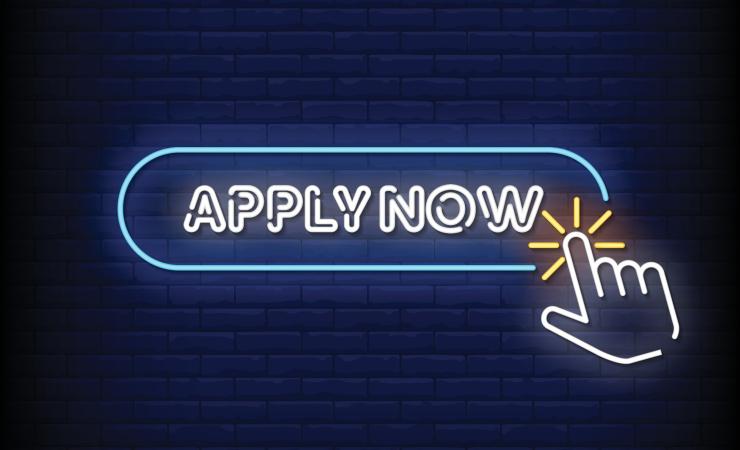 White neon lights say 'APPLY NOW' and a neon hand is clicking on this. THe background is dark blue tiles. 