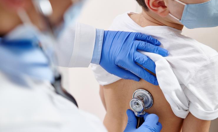 A doctor listens to a child's lungs via a stethoscope. Image by Taras Grebinets via Shutterstock