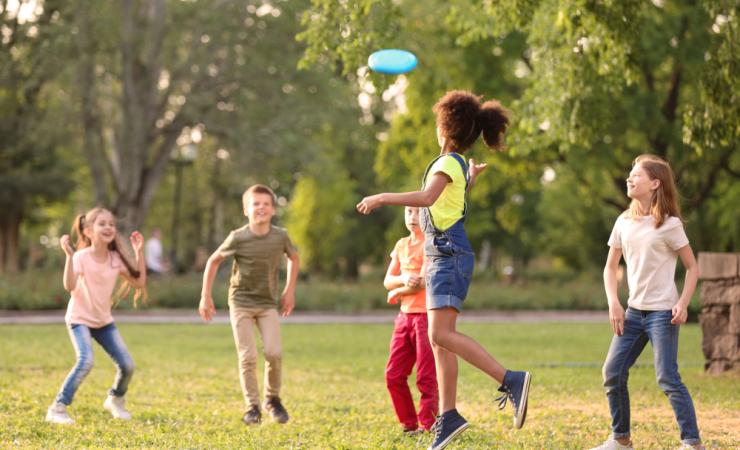 A group of 5 children playing frisbee in a park on a sunny day. Image by New Africa via Shutterstock.