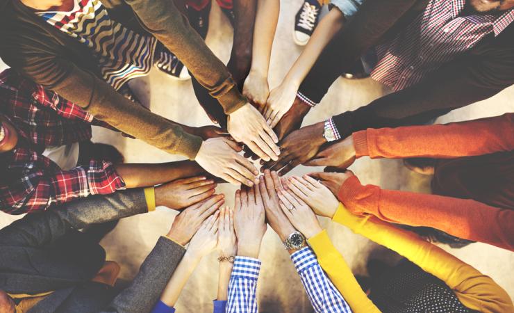 Multiple people's hands reaching together as viewed from above. Image by Rawpixel.com via Shutterstock