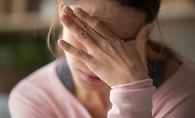 A woman holds her head in her hand. Image by fizkes via Shutterstock