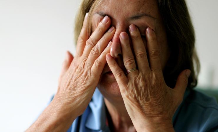 A tired woman rubs her eyes and face with her fingers. She has tanned skin, dark blond hair and a blue shirt. Image by Bricolage via Shutterstock
