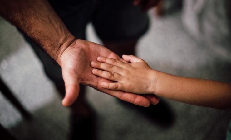 A child places their left hand on the upturned palm of a man's right hand. Image by Juan Pablo Serrano Arenas via Pexels.