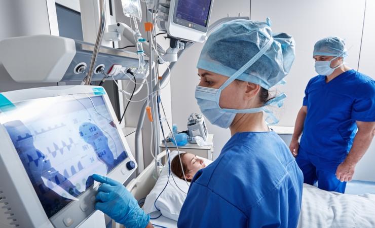 A healthcare worker working at a machine in an intensive care unit. Image by Peakstock via Shutterstock.