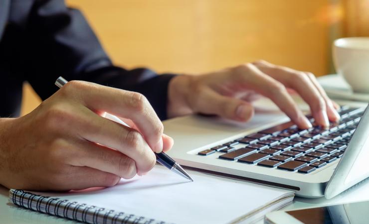 A person using a laptop and taking notes. Image by mrmohock via Shutterstock