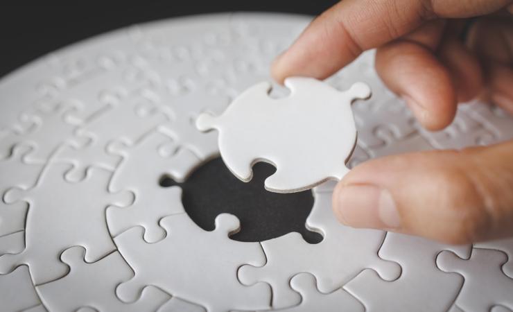 A person completing a jigsaw puzzle by placing the last piece in the centre. Image by Tinnakorn jorruang via Shutterstock.