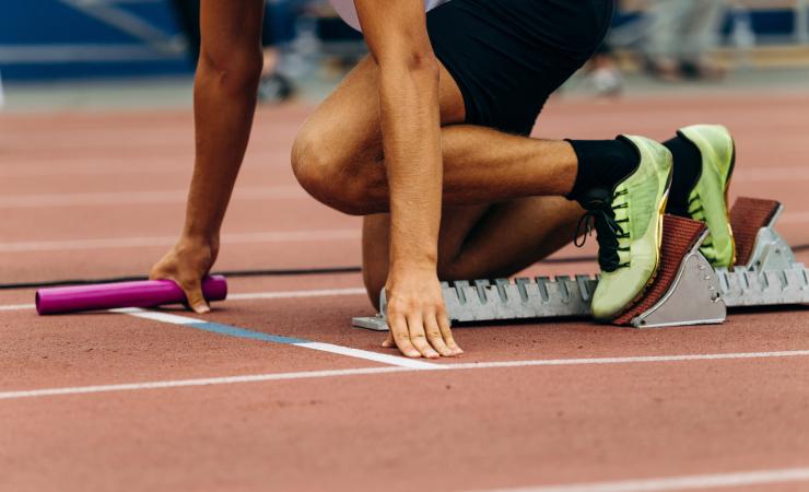 A sprinter at the start of a relay race. Their shoes are bright yellow/green and the baton is pink