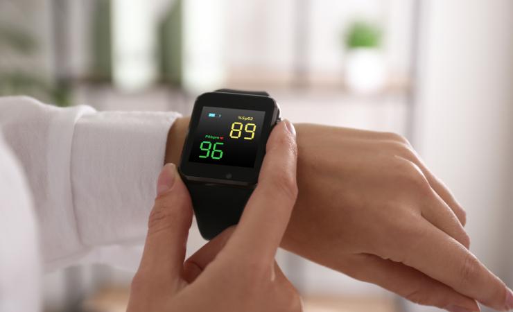 Close-up of a woman measuring oxygen levels with a smartwatch. The watch is on her left arm and she is holding the black watch with the thumb and index finger of her right hand. Image by New Africa via Shutterstock