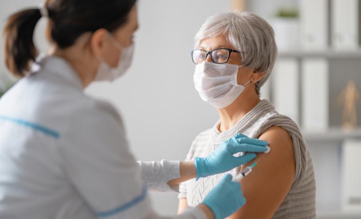 A doctor giving a senior woman a vaccination. They are both wearing facemasks. Image by Yuganov Konstantin via Shutterstock.