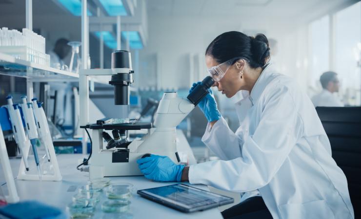 Woman looking down a microscope in the lab. Image by Gorodenkoff via Shutterstock