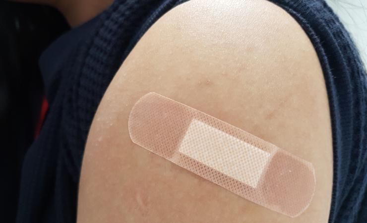 Close-up of a band aid on the upper arm. Image courtesy of Chanita Chokchaikul via Shutterstock