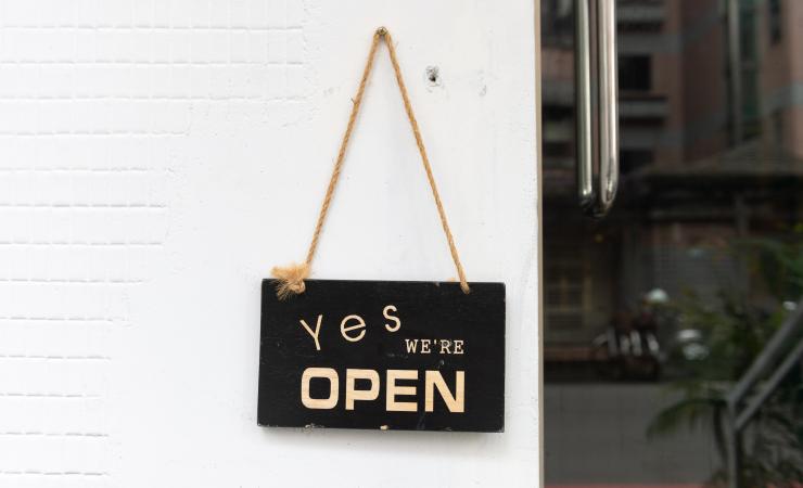 Sign hanging on a board that reads 'Yes we're open'. Image by Robbin Lee via Shutterstock