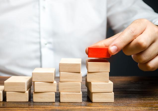 A man is building a ladder or growth chart from blocks. Image via Adobe by Andrii Yalanskyi