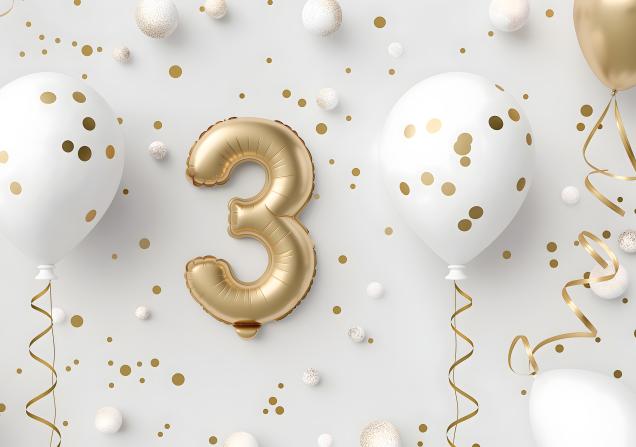 A golden balloon of the number three, against a white background with glitter and other white balloons. Image credit: AdobeStock_833782779