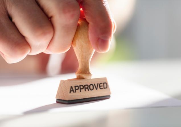 A hand stamping something with an 'APPROVED' stamp. Image by Brian A Jackson via Shutterstock.