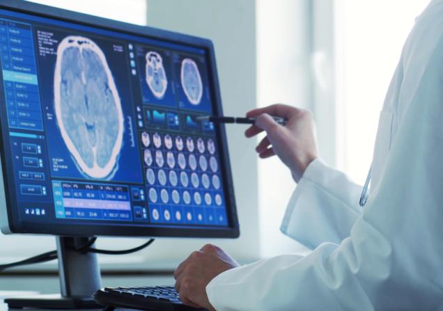 A doctor looking at a brain scan on a screen. Image by Max Acronym via Shutterstock