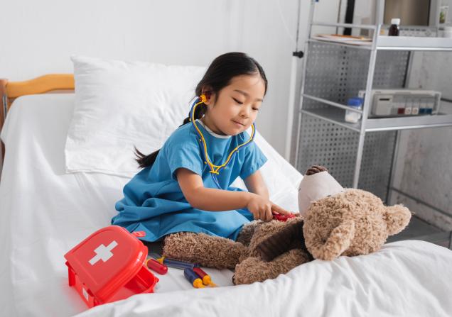 A girl using a stethoscope on a teddy. Image by Lightfield Studios via Adobe Stock.