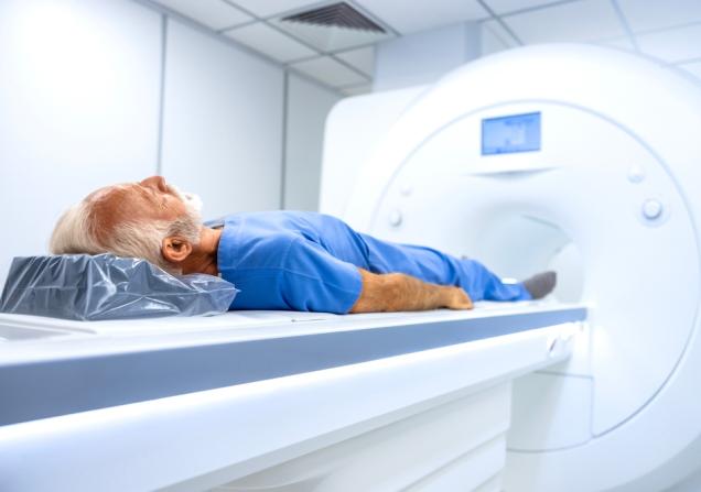 An elderly man who is about to have an MRI scan. He has white hair and a beard and is wearing what looks like blue, hospital issue pyjamas. Image by Aleksandar Malivuk via Shutterstock
