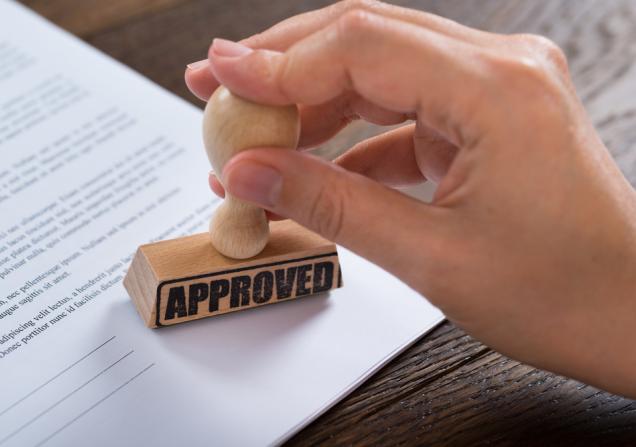 A hand using an 'approved' stamp on a document. 