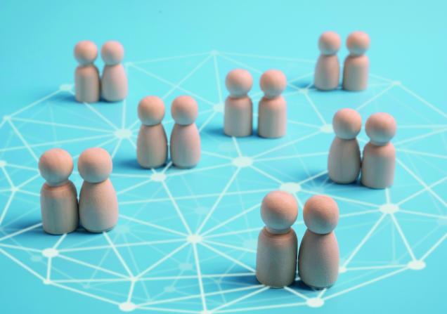 Little wooden figures networking on a bright blue background. Image via Shutterstock.