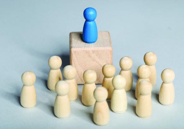 Wooden figures surrounding one figure on a platform. Image credit: 5 second studio via Shutterstock.