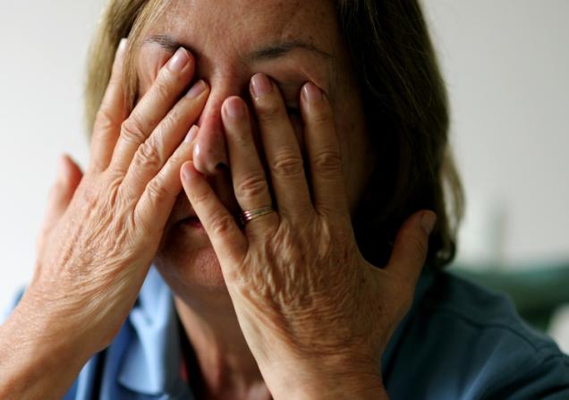 A tired woman rubs her eyes and face with her fingers. She has tanned skin, dark blond hair and a blue shirt. Image by Bricolage via Shutterstock