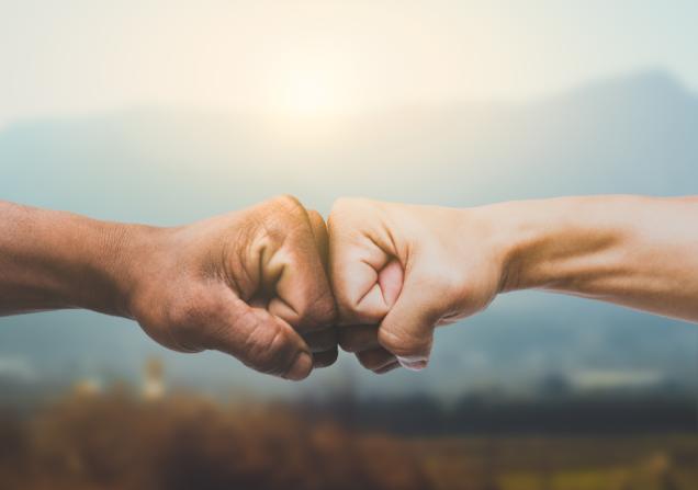 Two people doing a fistbump against a mountain backdrop. Image by Pasuwan via Shutterstock