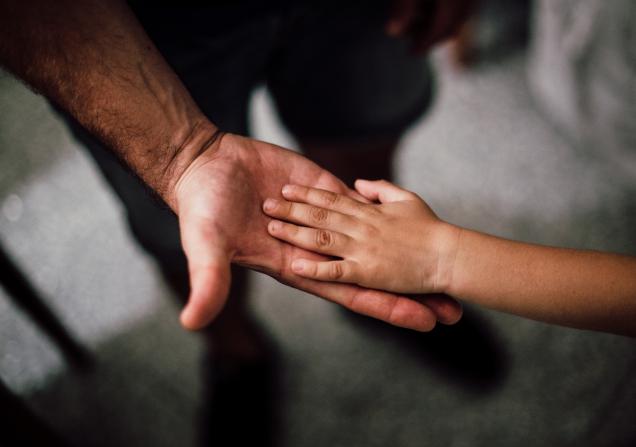 A child places their left hand on the upturned palm of a man's right hand. Image by Juan Pablo Serrano Arenas via Pexels.
