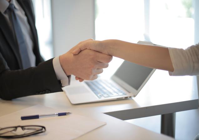 Two people shaking hands across a desk. Image by Andrea Piacquadio via Pexels.