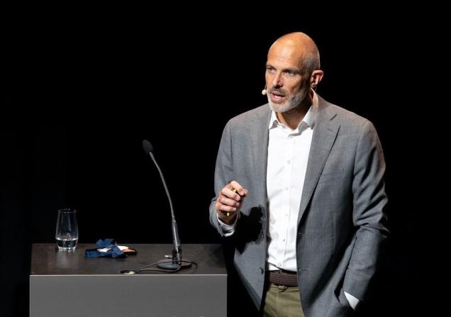 Niklas Blomberg speaking at an event last year. He is wearing a grey jacket and white shirt and is standing next to a black lectern with a microphone on it. Image courtesy of ELIXIR.