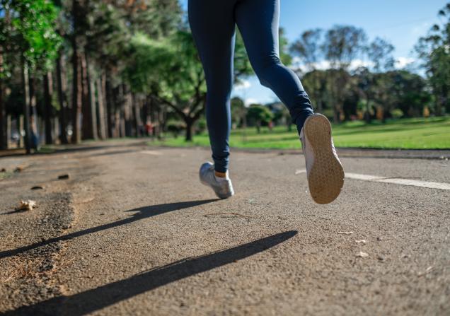 The legs of a person jogging. They're wearing blue leggings and trainers and they're jogging along a road with grass on the right and trees on the left. Image by Daniel Reche via Pexels