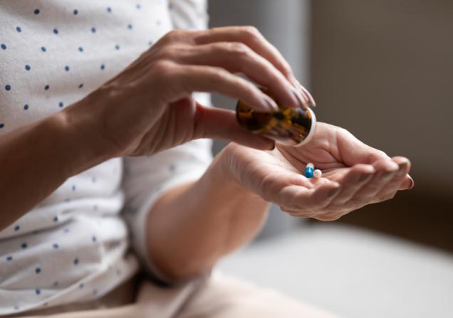 A woman in a white top with black spots is tipping a pill from a little brown medicine bottle into her hand. Image by fizkes via Shutterstock
